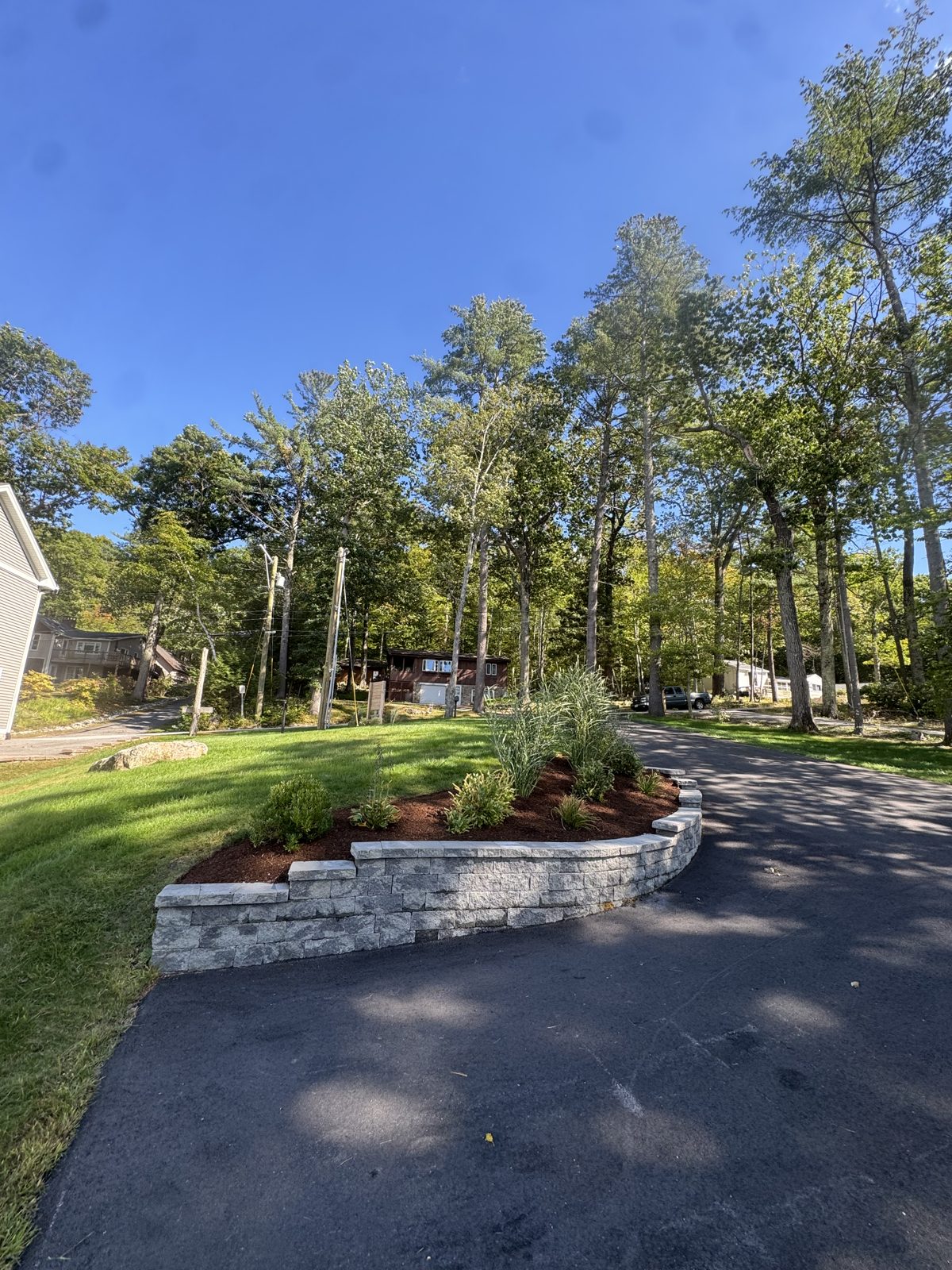 Stone retaining wall and planted bed at the edge of a paved driveway
