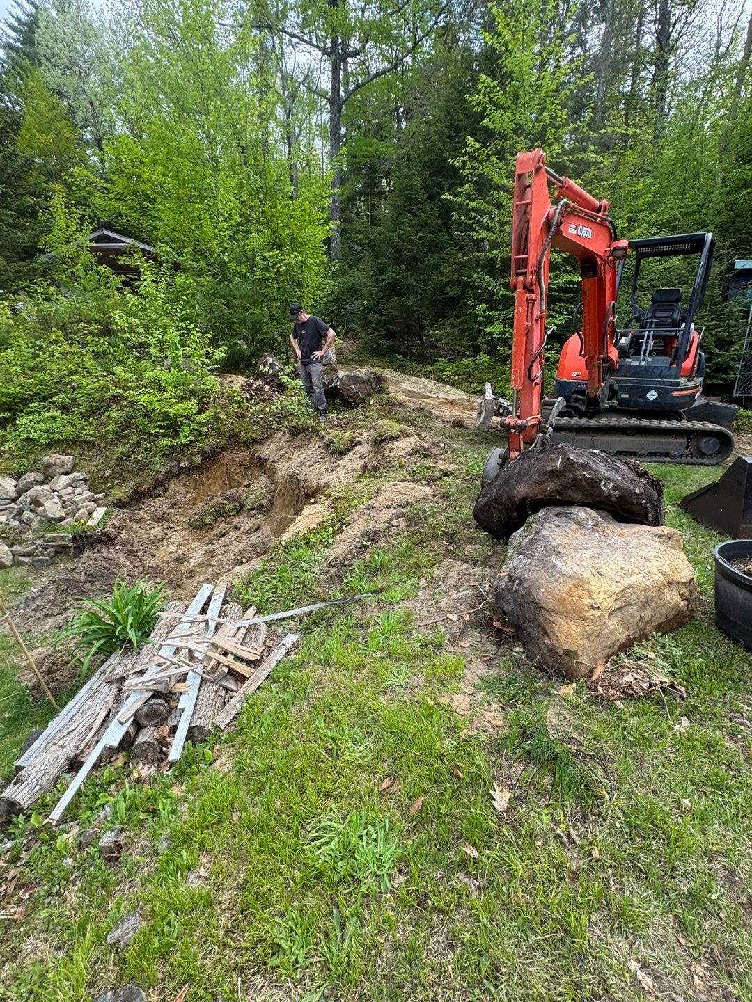 Compact excavator grading soil for a new gravel driveway in the woods