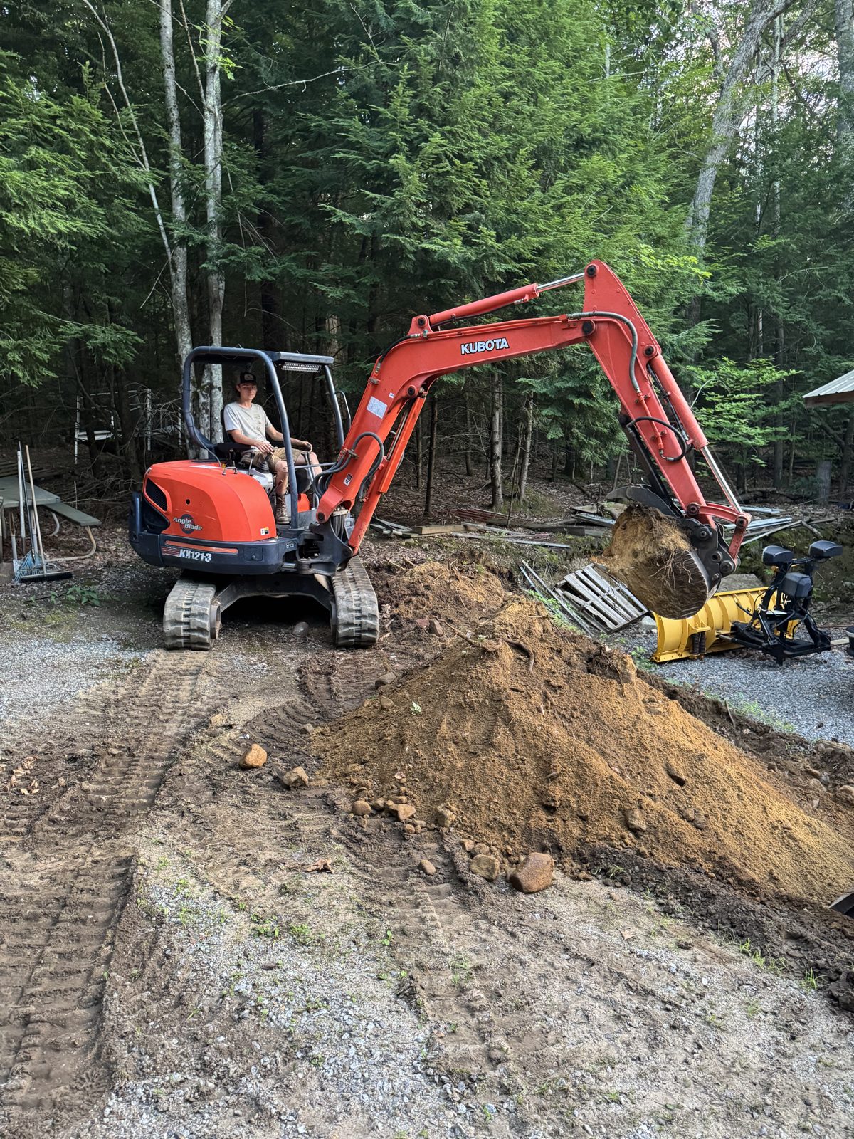 Mini excavator digging and piling dirt on a wooded site