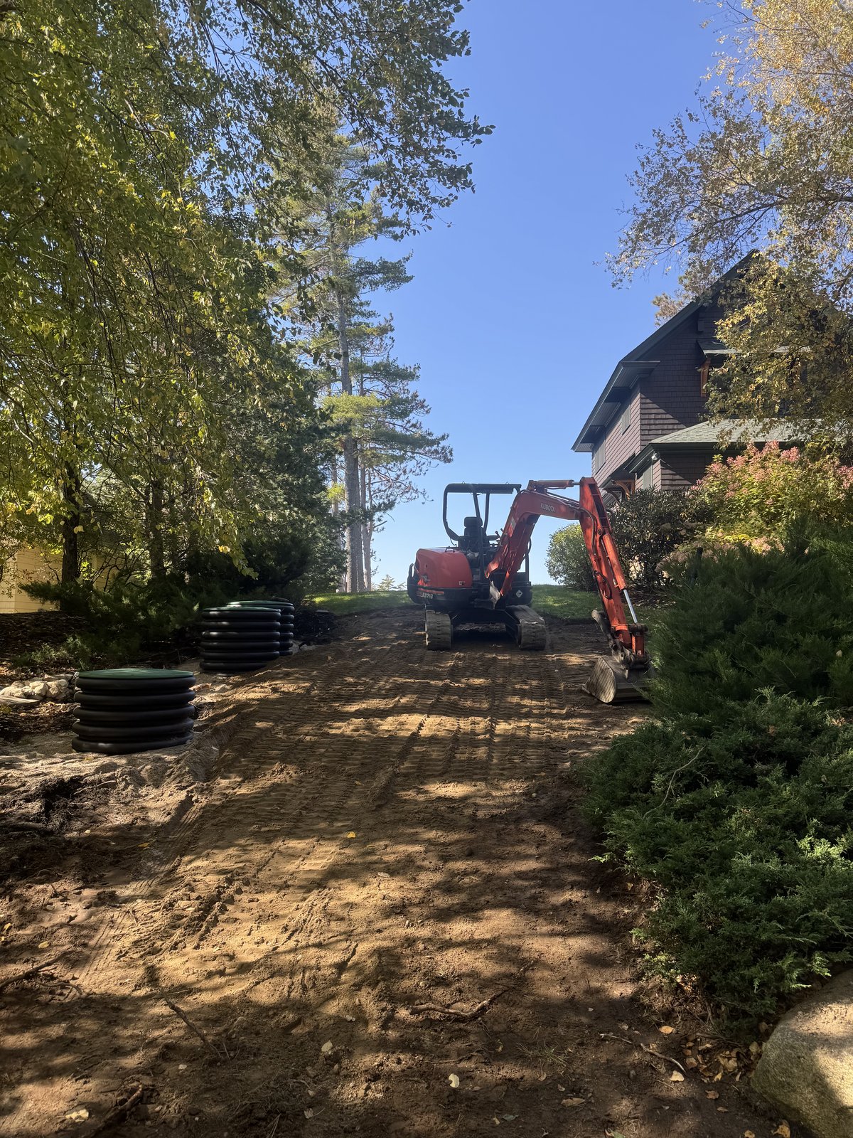 Mini excavator grading a dirt path beside a home during a septic repair