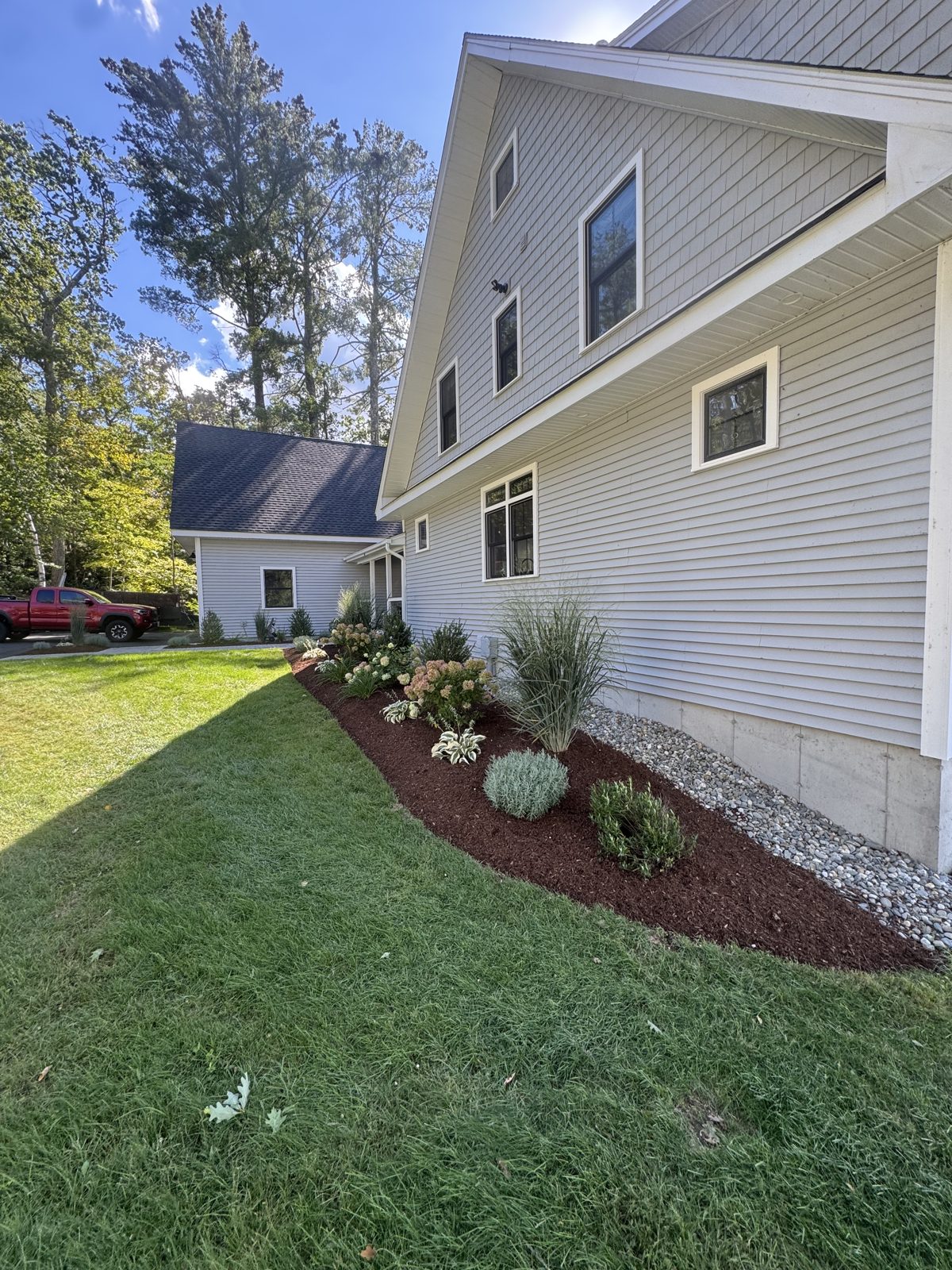 Mulched side yard bed with shrubs and white stone along a house