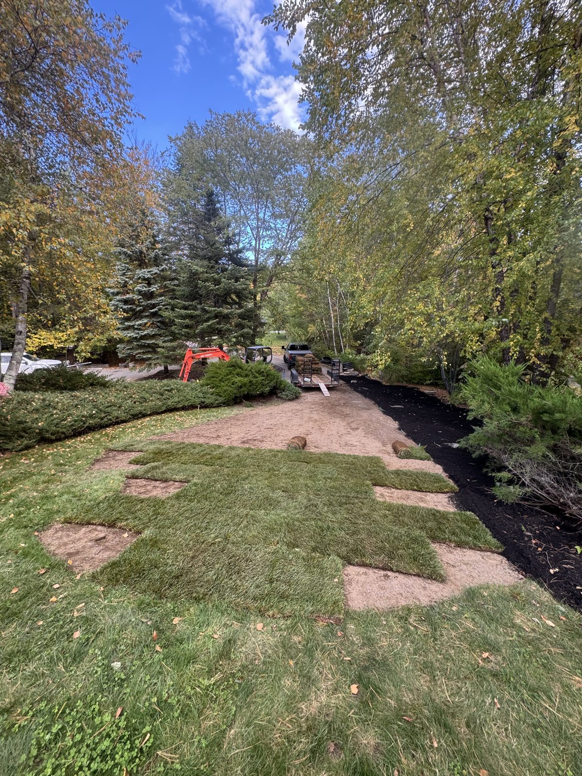 Sod rolls being laid across a graded back yard